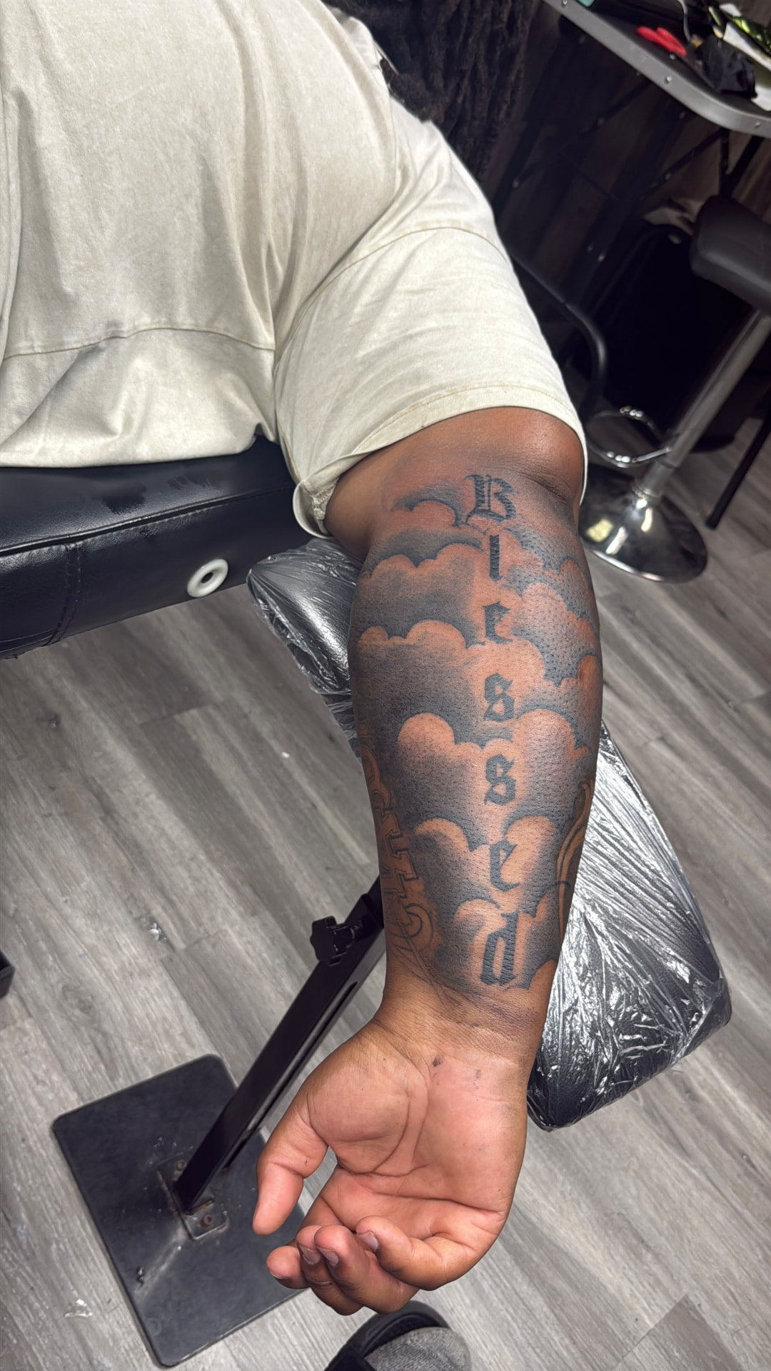 "Blessed" lettering with clouds forearm tattoo